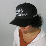 Person wearing a black cap with 'daddy princess' text on a plain background