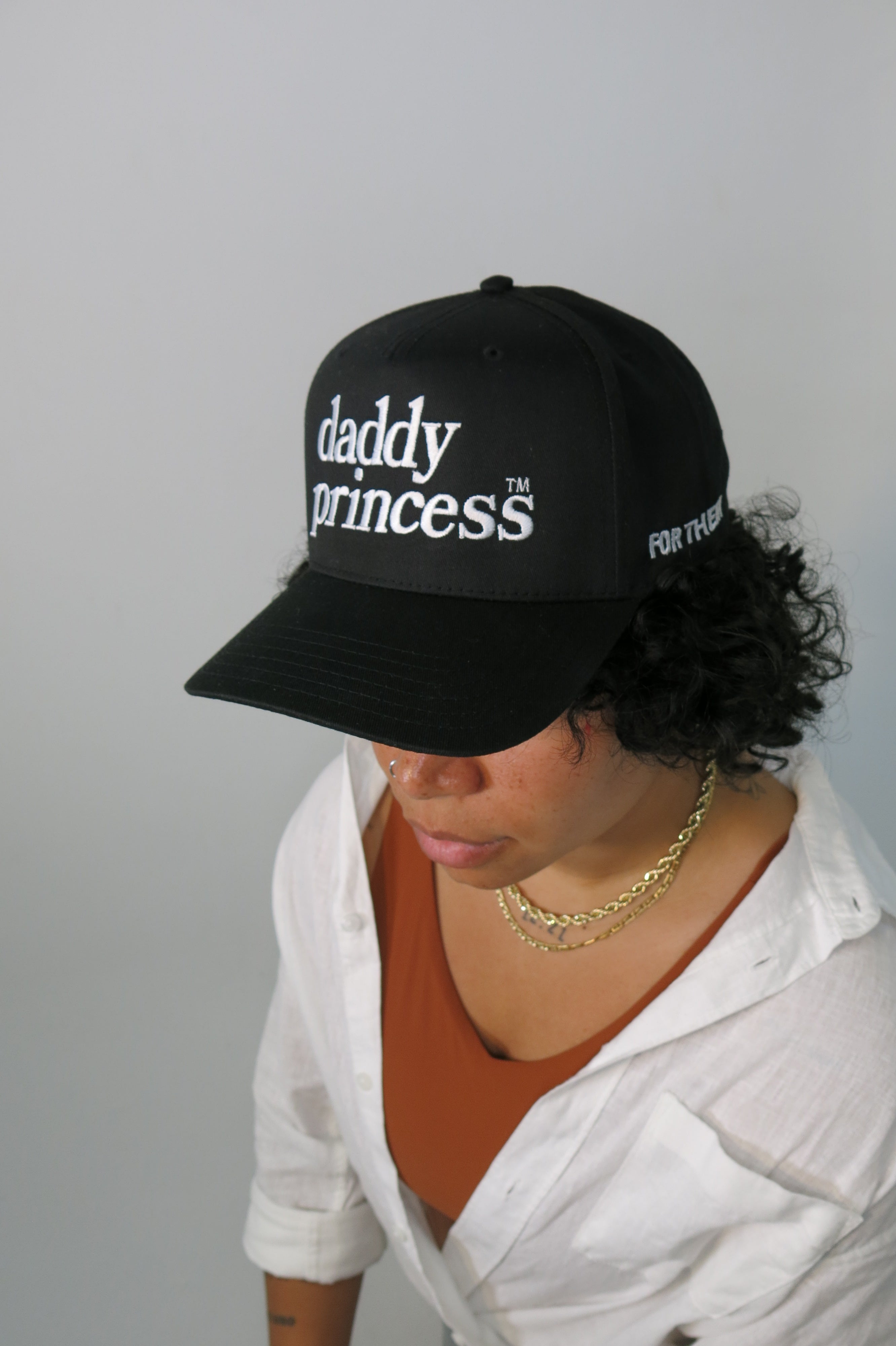 Person wearing a black cap with 'daddy princess' text on a plain background